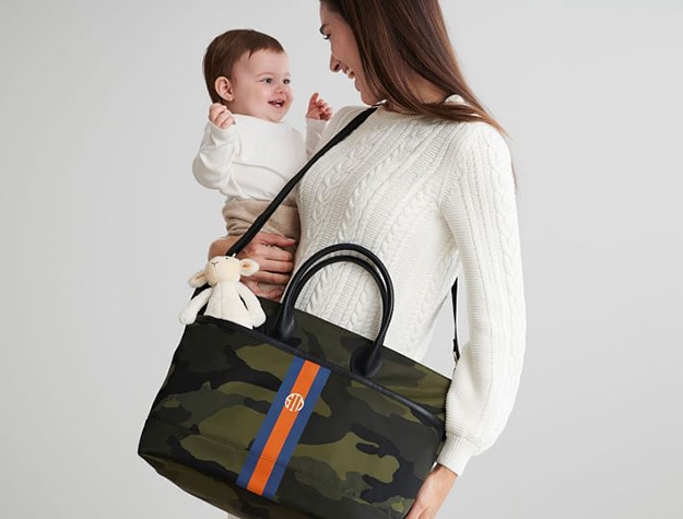 Woman holding a baby and wearing Mark & Graham camo diaper bag.