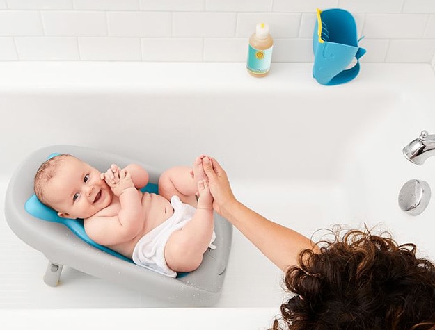 Mother preparing to wash a baby in a baby tub placed inside a bathtub.