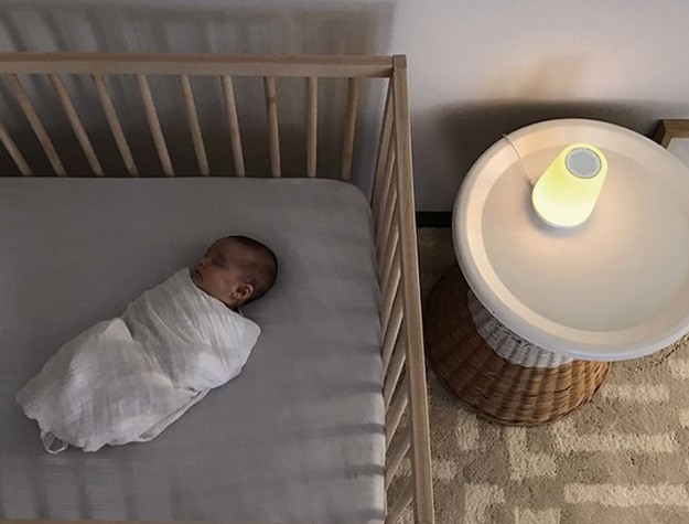 Baby sleeps in a crib next to a glowing sound machine.