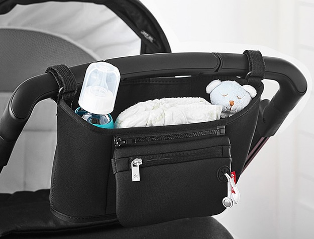 Black stroller caddy containing stuffed animal, diapers, bottle and ear buds.