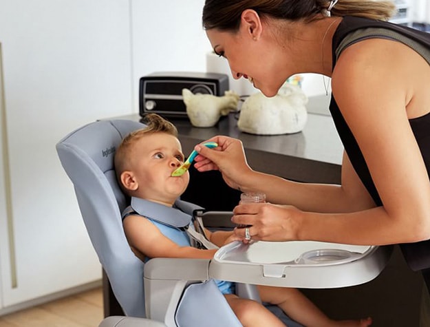 Mother feeding a baby sitting in a high chair.