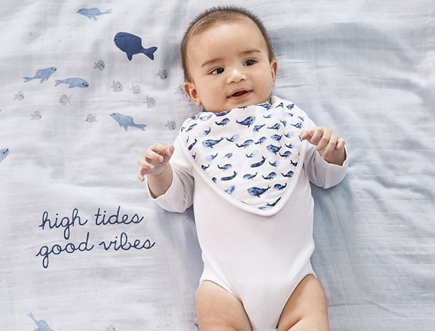 Baby lying on a nautical-themed blanket wearing a whale print drool bib.