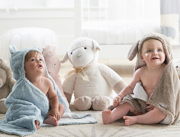 Two babies in hooded towels with stuffed animals.