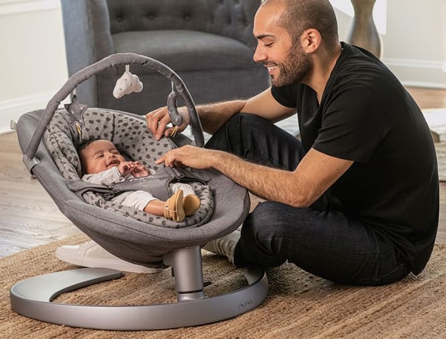Father playing with a baby strapped into a bouncer chair.