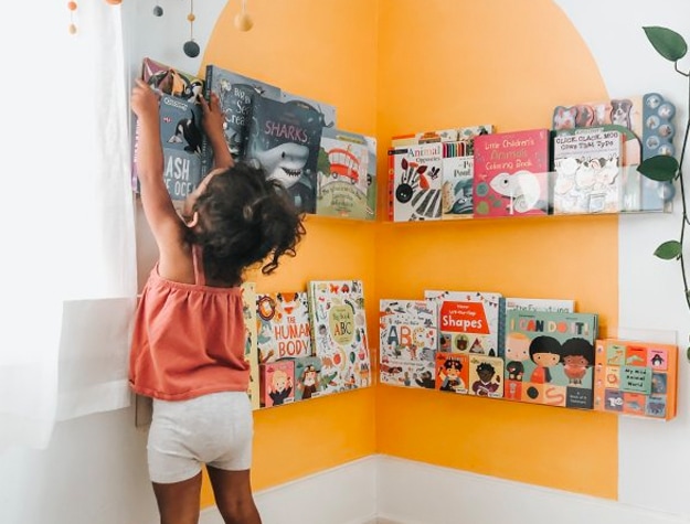 Little girl taking book from corner wall shelf