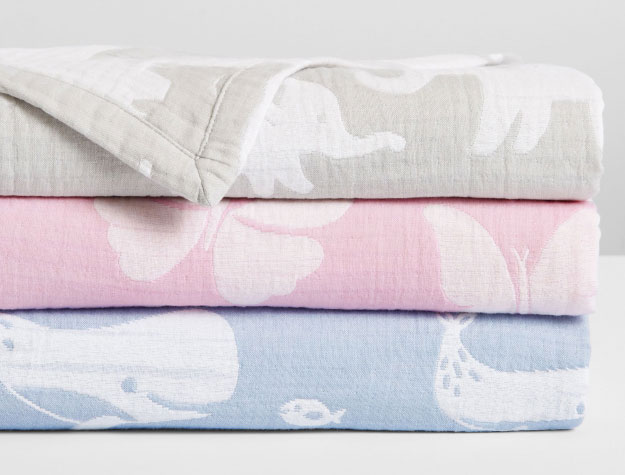 A stack of folded, colorful Organic Muslin Baby Blankets.