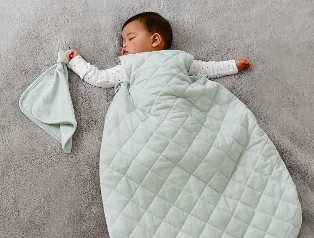 Baby sleeping on a floor wrapped in green quilted sleep sack.