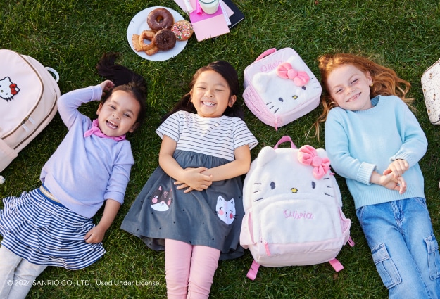 A group of young girls lay in the grass at school surrounded by their Hello Kitty backpacks and lunch boxes.