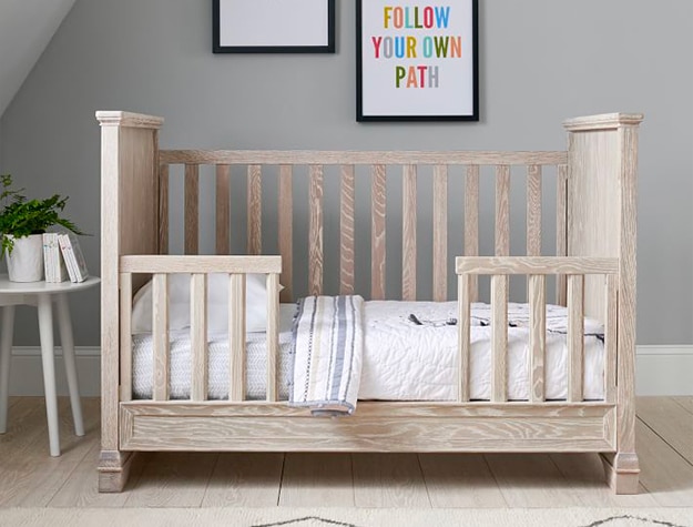 A light brown toddler bed with white bedding. A light brown toddler bed with white bedding.