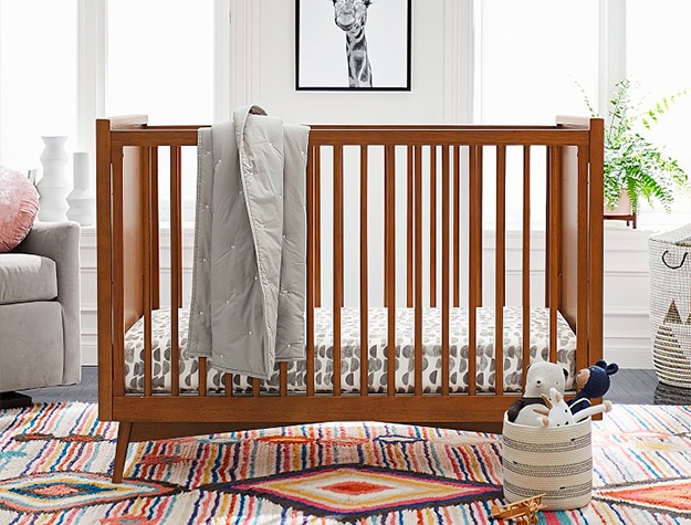A brown crib in a nursery with a gray blanket hung on its side. A brown crib in a nursery with a gray blanket hung on its side.