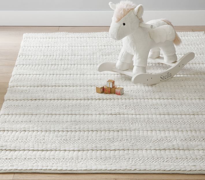 A white flatweave rug with a white wooden unicorn placed on it.