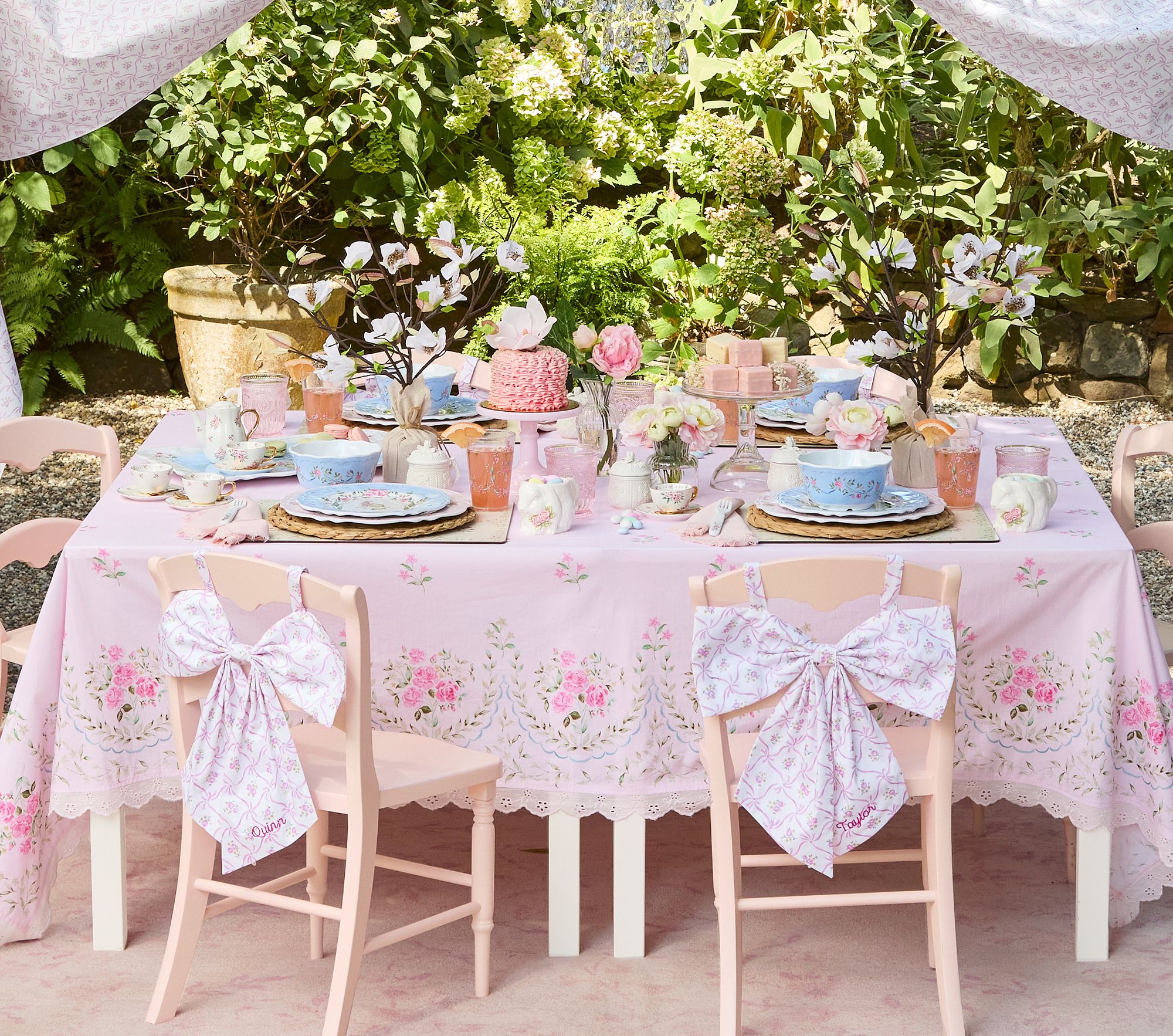 Table set with pink floral bow chairbackers on chairs under a canopy.