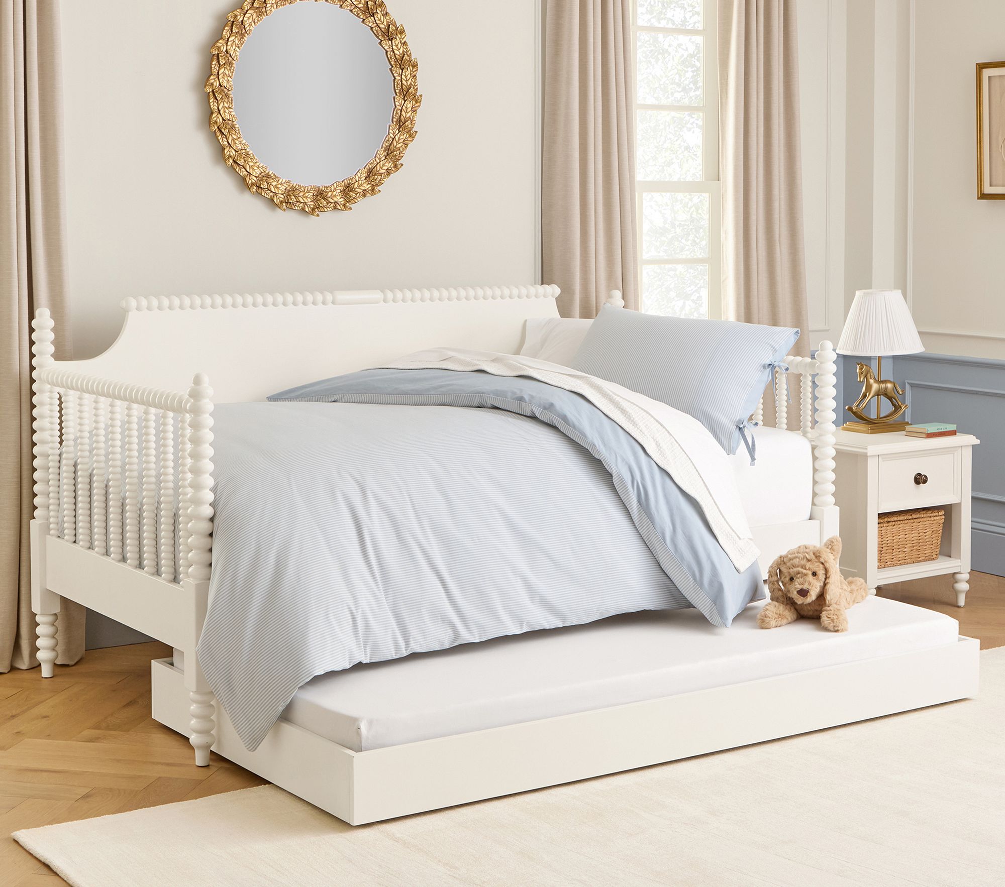 White bed frame with turned posts and light blue bedding in a bright room