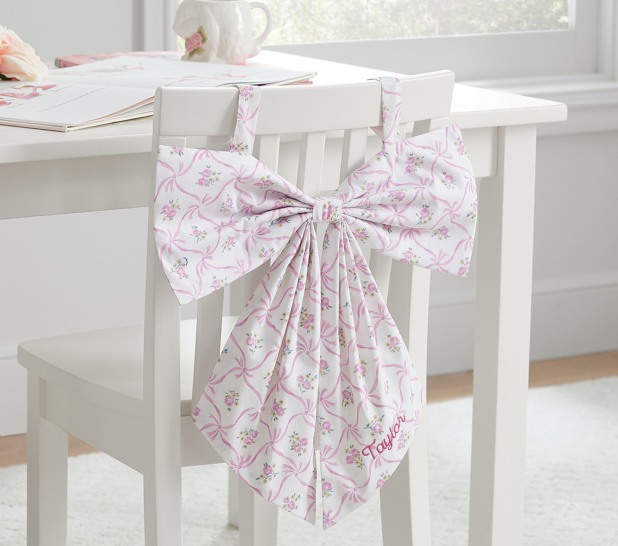 Close-up of pink floral bow chairbacker showing bow, straps, and embroidered name Taylor.