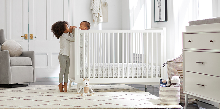 An older sister greeting her baby sibling in their crib.