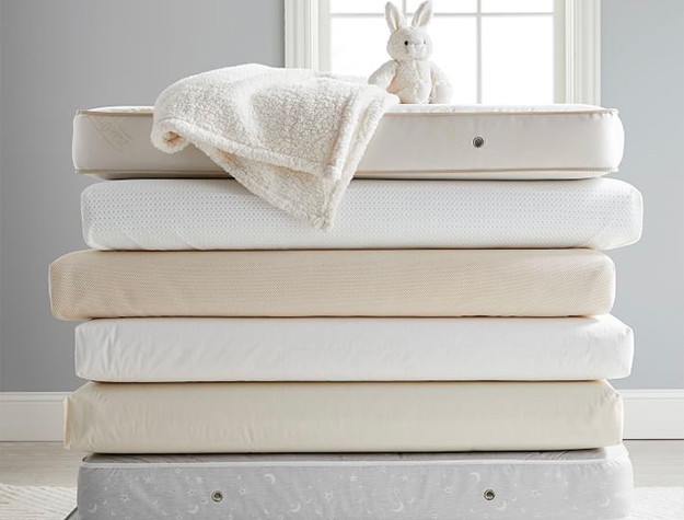 A stack of crib mattresses with a stuffed rabbit and a blanket on top.
