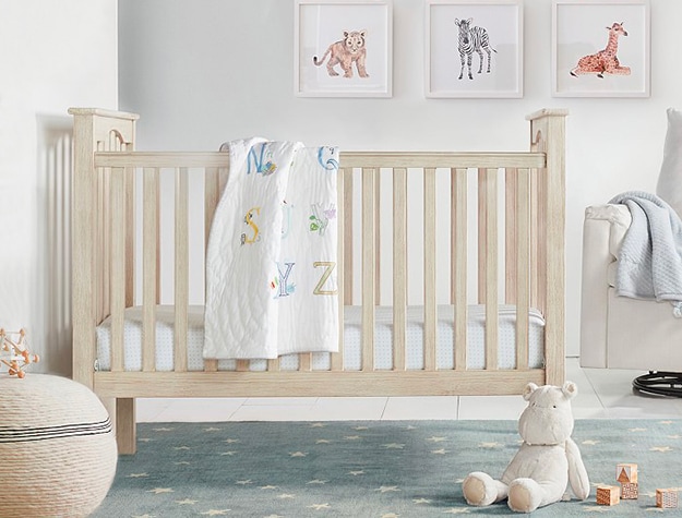 Wooden crib with alphabet blanket hanging on it.