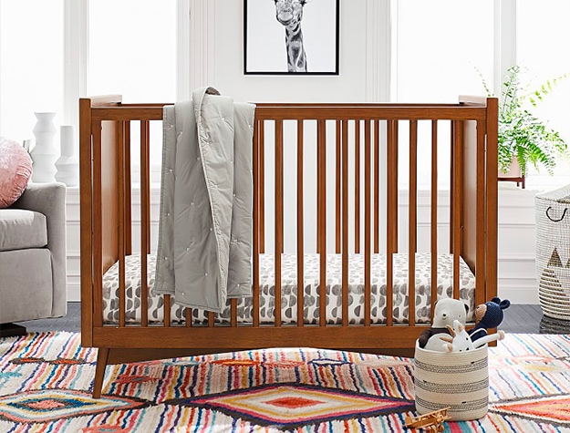 A brown crib in a nursery with a gray blanket hung on its side.