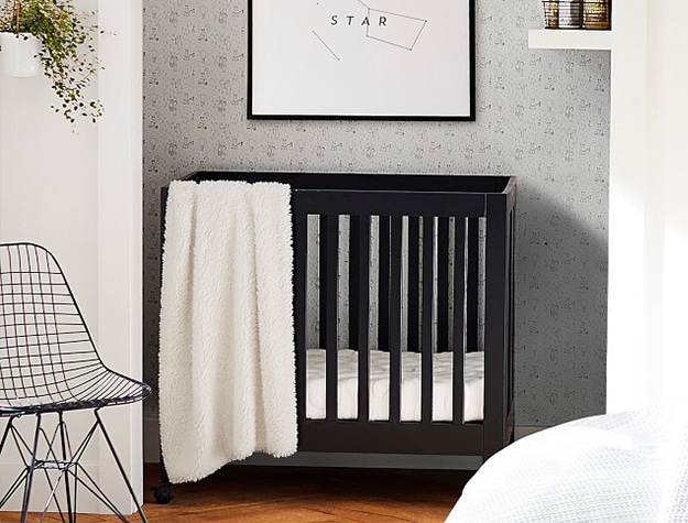 A black miniature crib tucked into the corner of a room.