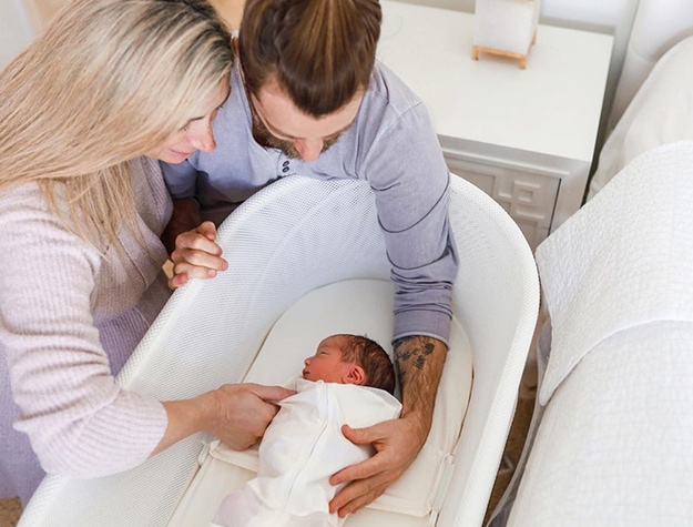Parents holding baby in bassinet