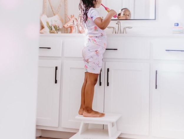 Little girl brushing her teeth standing on a step stool