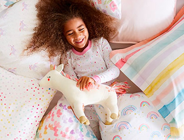 Child holding unicorn stuffed animal on pile of pillows