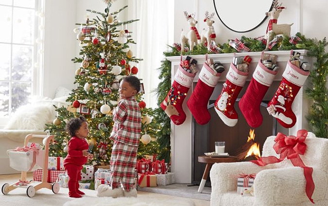  Two young children standing in front of a fireplace with five stuffed stockings