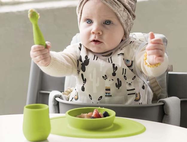 A baby in a highchair eating with the EZPZ first foods set