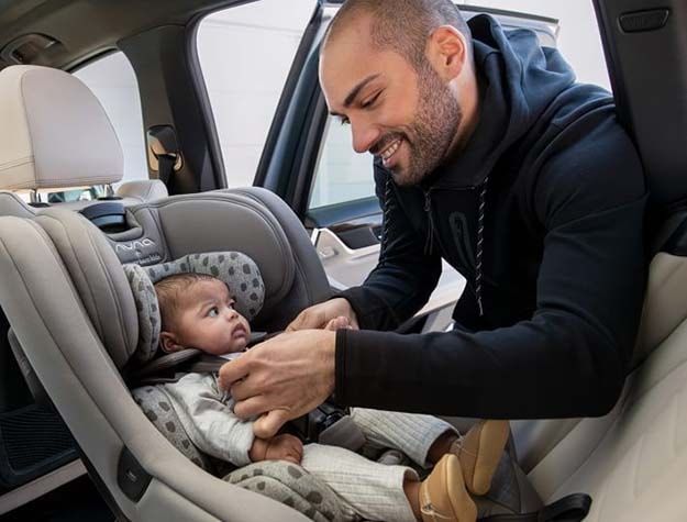 A man buckling a baby into the Nuna Rava convertible car seat