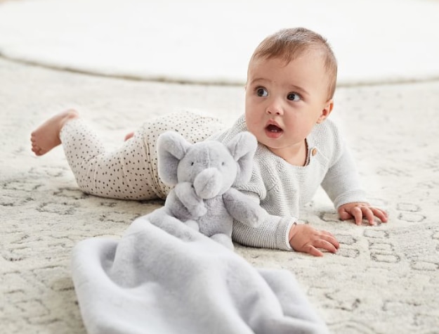 baby lying on tummy next to a gray elephant-themed lovey 