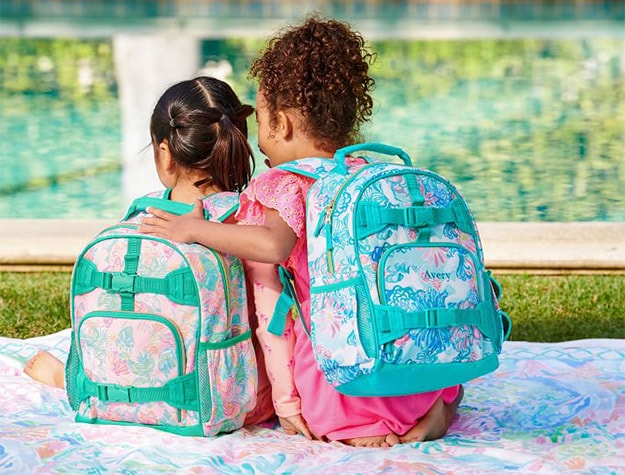 Two children on a blanket wearing Mackenzie Lilly Pulitzer Unicorn In Bloom backpacks.