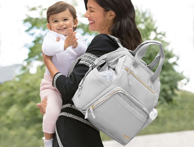 Mother holding baby and wearing the Skip Hop Mainframe Wide Open Backpack Diaper Bag.