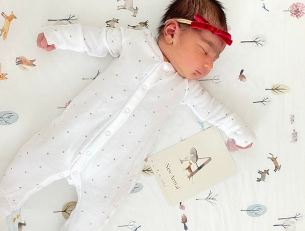 Baby lying on Dakota woodland crib sheet next to card reading new arrival.