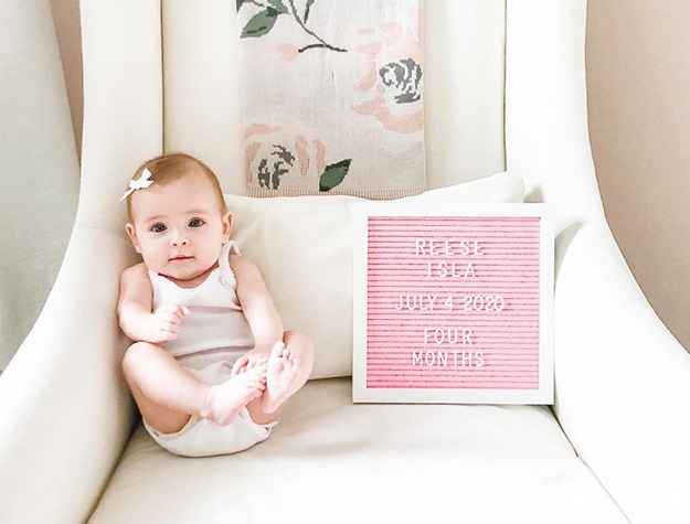 Baby sitting on Merced nursery glider beside a letter board reading Reese Isla July 4 2020 four months.