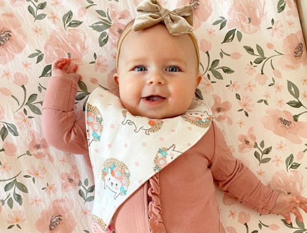 Baby lying on Meredith all-over floral organic crib blanket in matching onesie.