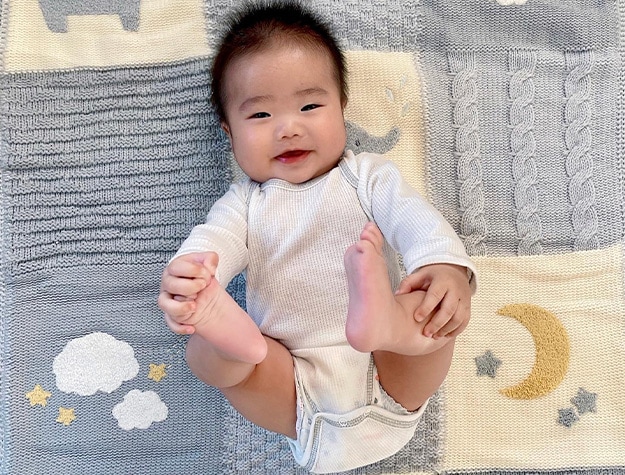 Smiling baby lying down on a hippo baby heirloom blanket.