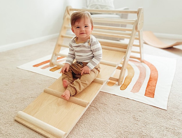 Child sitting on little climber reversible ladder slide set in a nursery.