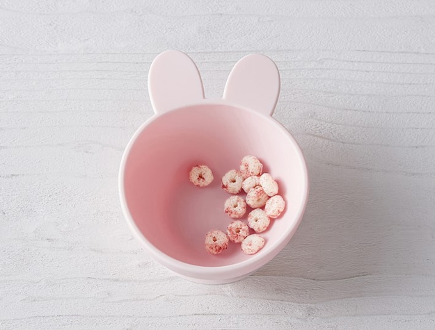 A pink suction silicone bowl with bunny ears holding snacks.