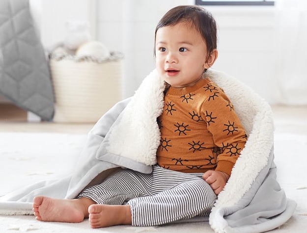 A baby wrapped in a Sherpa Baby Blanket on the floor.