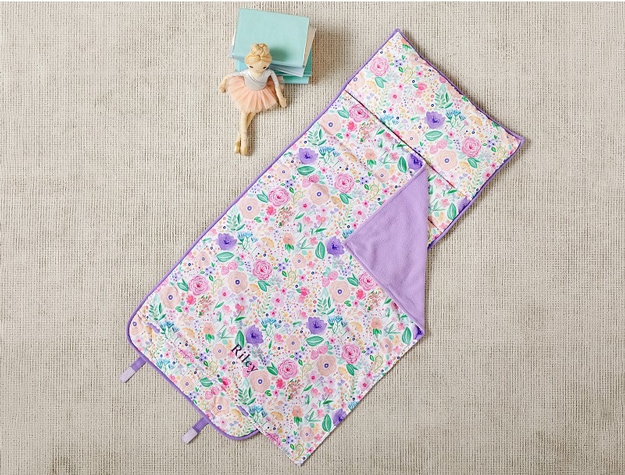 A doll next to a stack of notebooks on the floor next to a personalized Mackenzie Lavender Floral Blooms Nap Mat.