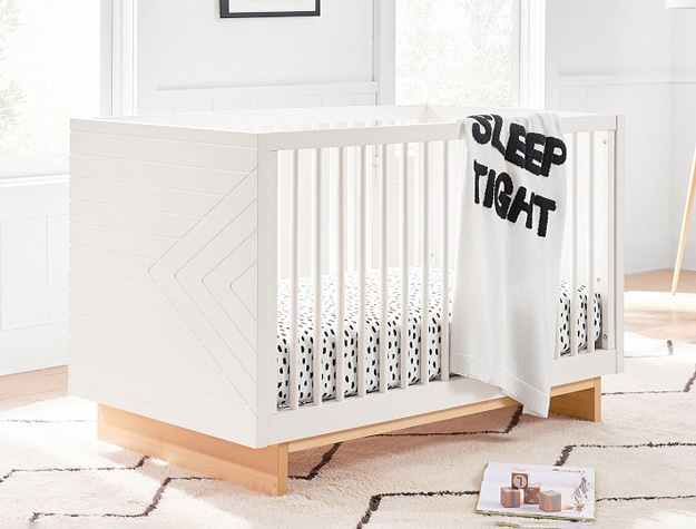 Cora Convertible Crib with a white “sleep tight” blanket hanging over it and animal-print sheets.
