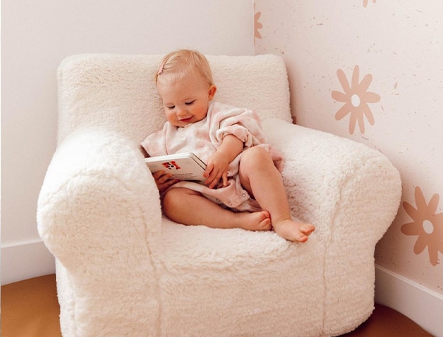 Baby sitting on an Anywhere Chair looking at a book.