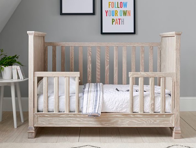 A light brown toddler bed with white bedding.