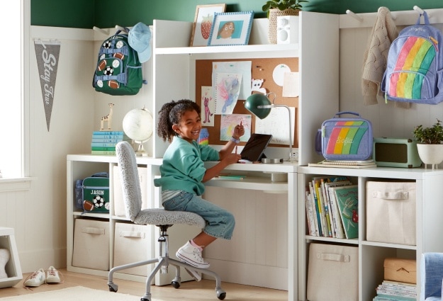 A young girl sits at her desk in her room, laughing and enjoying herself.