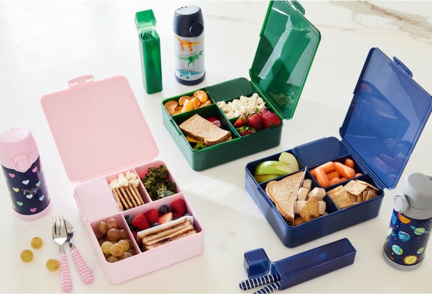 Group shot of the all-in-one bento box food containers in a variety of colors – pink, blue, and green – alongside utensil cases and water bottles.