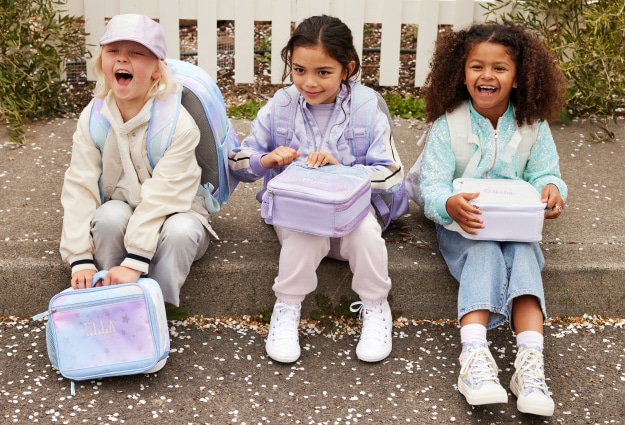 A group of girls sit on the sidewalk with their Pottery Barn Kids lunch boxes out, ready to eat lunch.