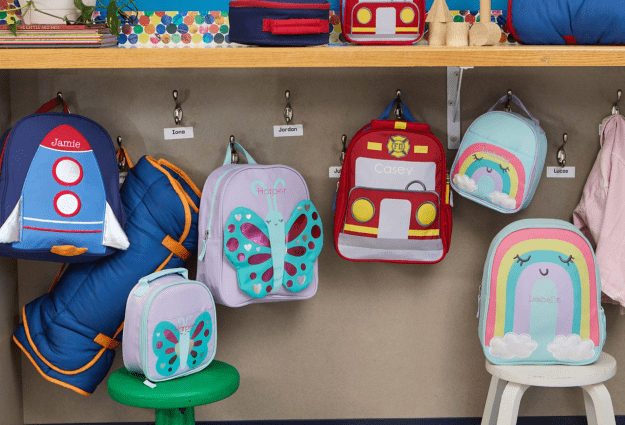 A group shot of Little Critter backpacks hanging from hooks inside a preschool classroom. 