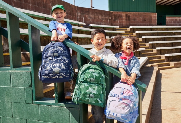 Three kids pose with their new backpacks on the first day of school.