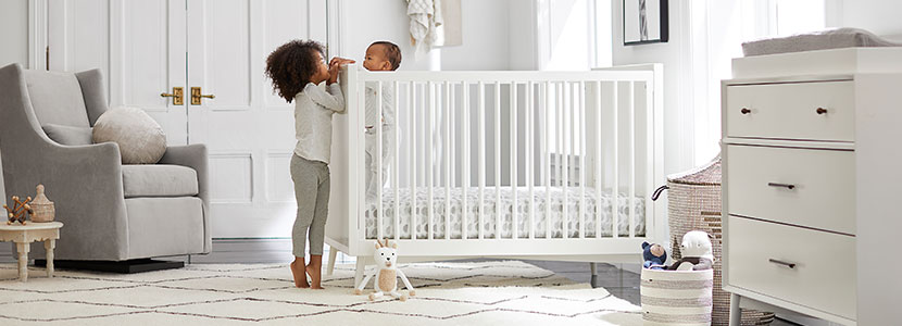 An older sister greeting her baby sibling in their crib.